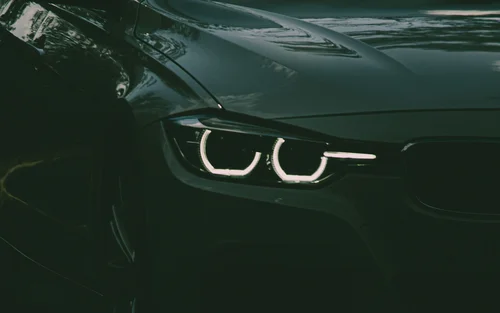 Book your holiday now. Off to South Tyrol! Front view of a black car with headlights on at night