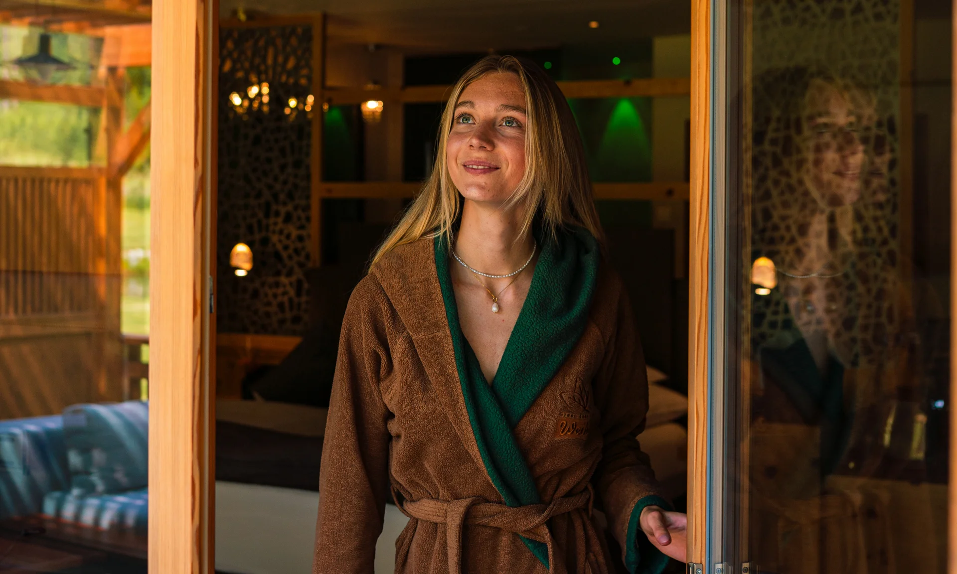 Entschleunigen und genießen in diesem Hotel nahe Bruneck Frau in braunem Bademantel öffnet Glastür in gemütlichem Holzhaus