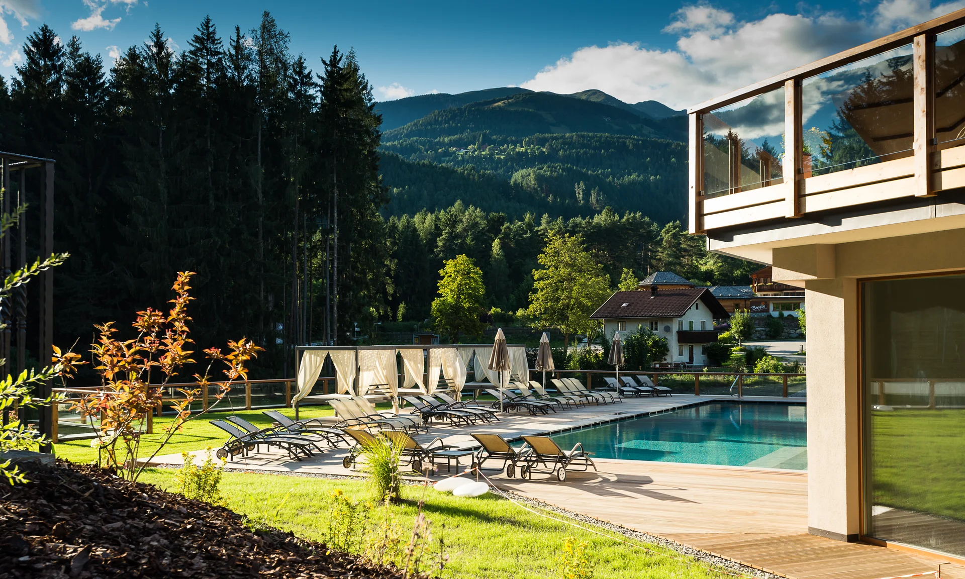 Entschleunigen und genießen in diesem Hotel nahe Bruneck Pool mit Liegestühlen und Bergblick an einem sonnigen Tag