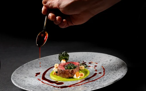 Book your holiday now. Off to South Tyrol! Hand drizzling sauce on artfully plated gourmet dish on gray plate