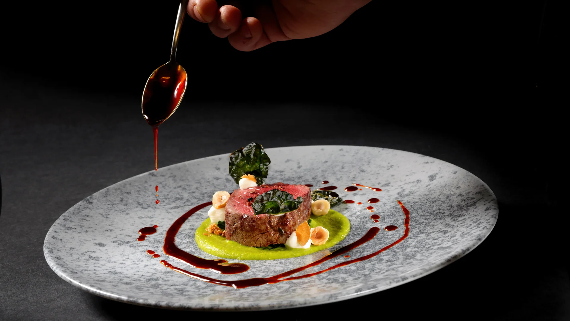 Entschleunigen und genießen in diesem Hotel nahe Bruneck Hand träufelt Sauce auf kunstvoll angerichtetes Gourmetgericht auf grauem Teller