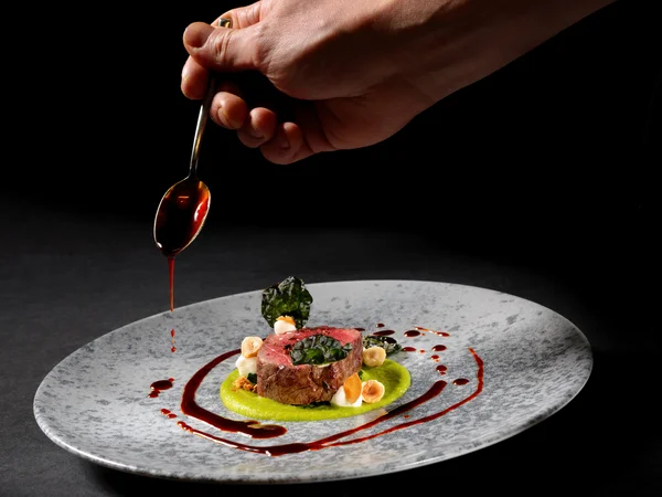 Entschleunigen und genießen in diesem Hotel nahe Bruneck Hand träufelt Sauce auf kunstvoll angerichtetes Gourmetgericht auf grauem Teller