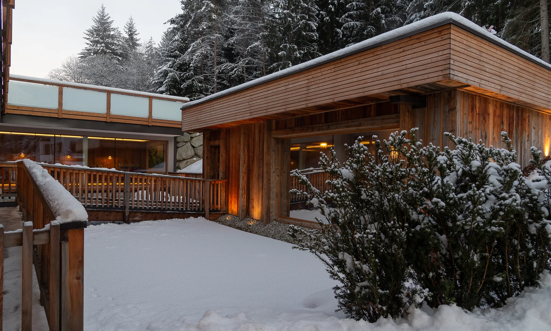 Entschleunigen und genießen in diesem Hotel nahe Bruneck Holzhaus mit verschneitem Garten und Büschen vor verschneitem Wald