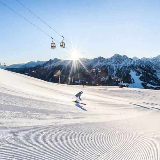 Entschleunigen und genießen in diesem Hotel nahe Bruneck Zwei Skifahrer auf einer sonnigen Piste mit Bergpanorama und Gondelbahn