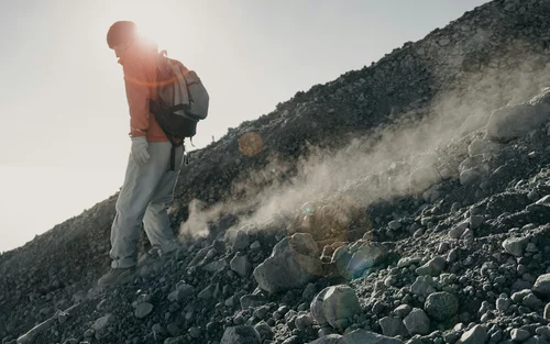 Book your holiday now. Off to South Tyrol! Person with backpack walking down dusty rocky slope in sunlight