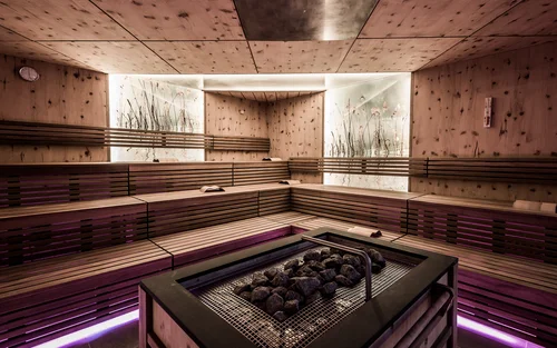 Book your holiday now. Off to South Tyrol! Modern sauna room with wooden benches and heated stones in the center