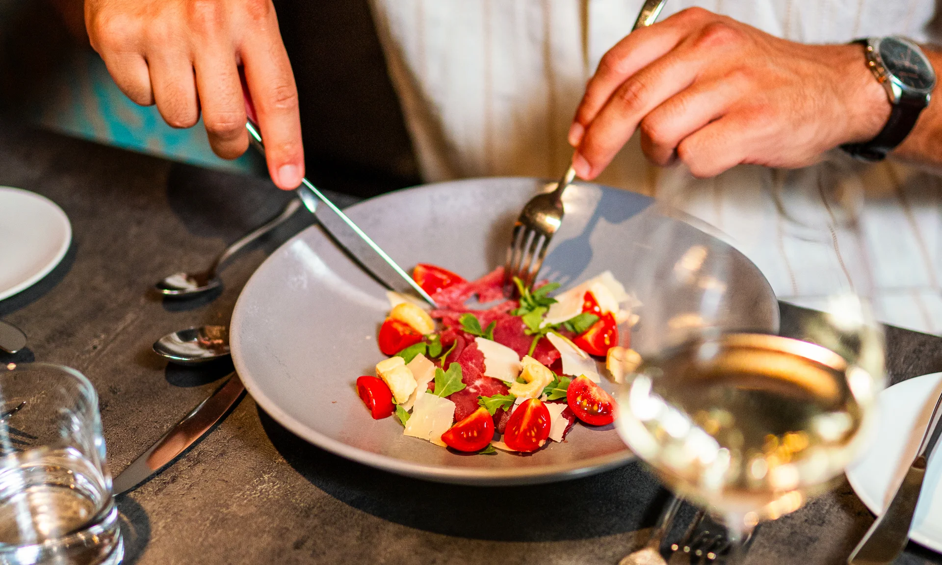Entschleunigen und genießen in diesem Hotel nahe Bruneck Person schneidet Salat mit Tomaten und Käse auf grauem Tisch