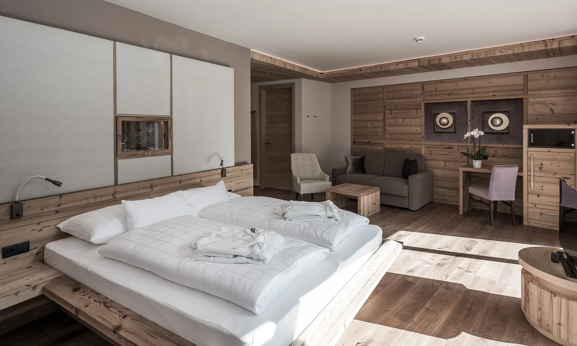 Entschleunigen und genießen in diesem Hotel nahe Bruneck Helles Hotelzimmer mit Doppelbett, Sofa und Holzmöbeln