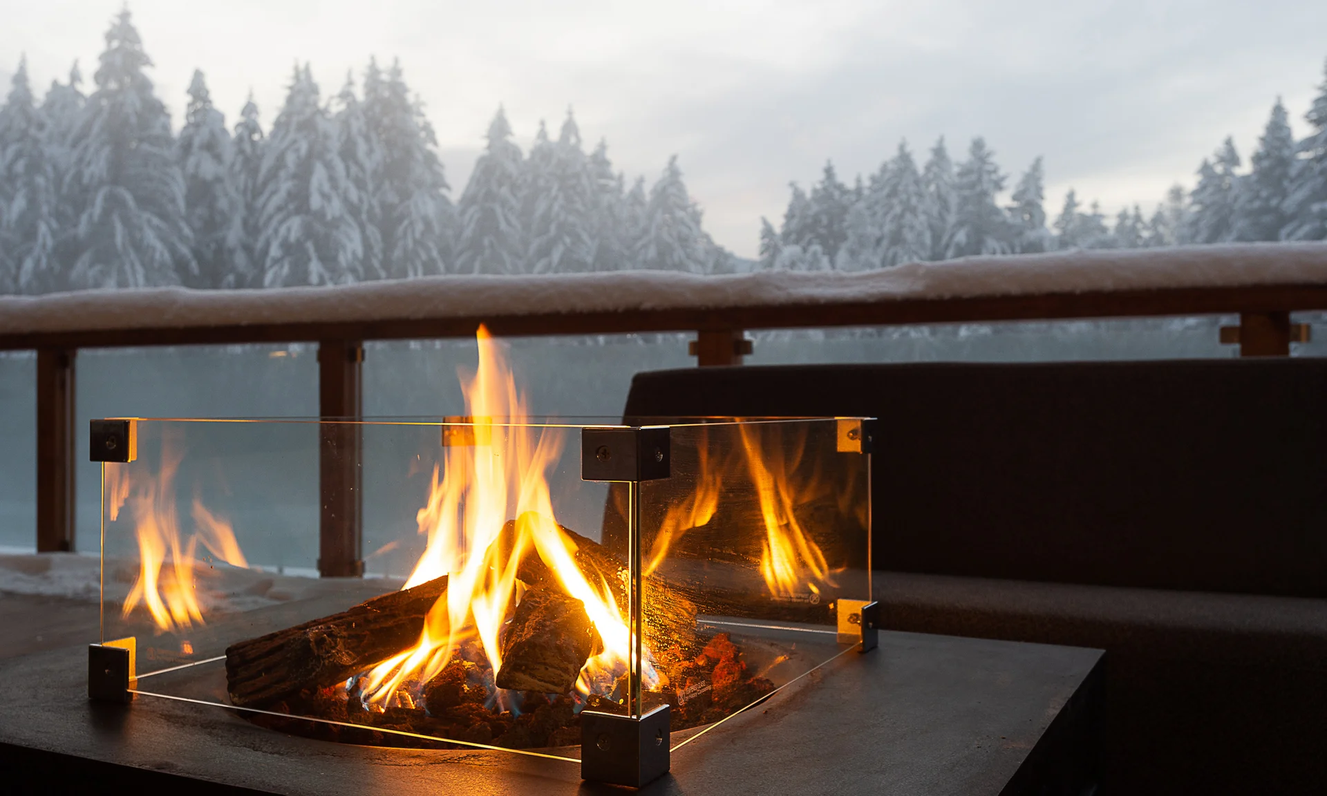 Entschleunigen und genießen in diesem Hotel nahe Bruneck Feuerstelle mit Glasumrandung auf Terrasse vor verschneitem Wald