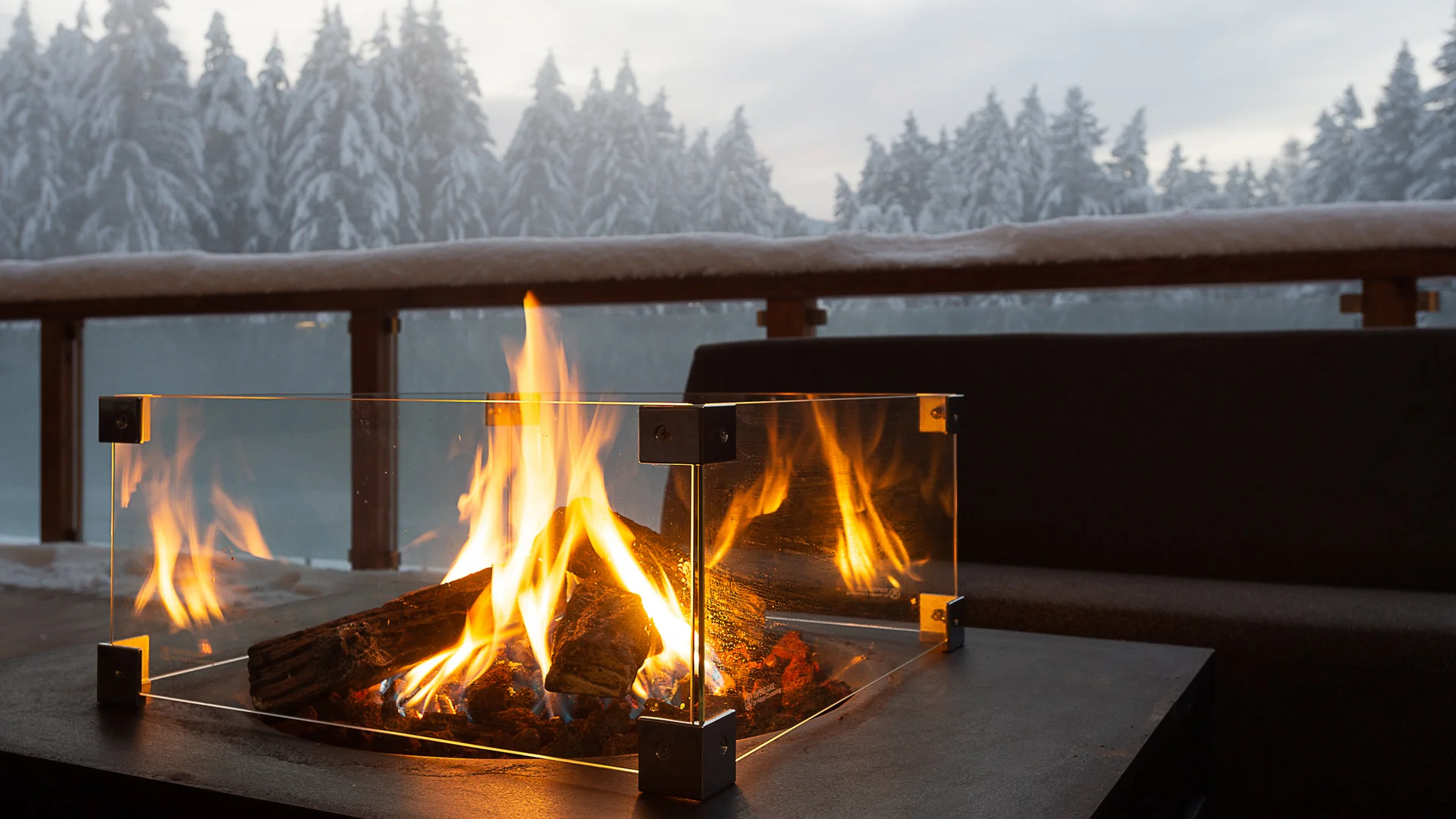 Entschleunigen und genießen in diesem Hotel nahe Bruneck Feuerstelle mit Glasumrandung auf Terrasse vor verschneitem Wald